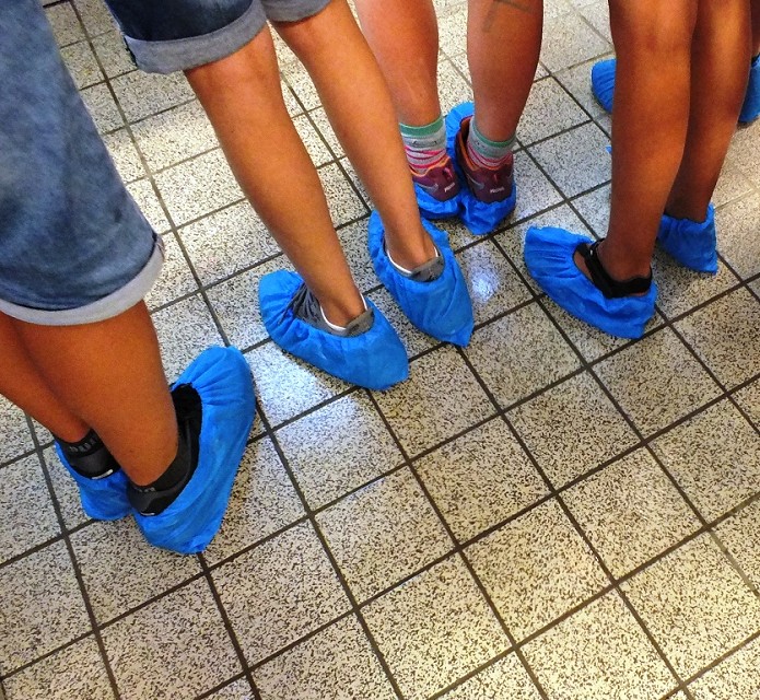 Schuhe von Teilnehmenden mit blauen Schutzüberzügen.